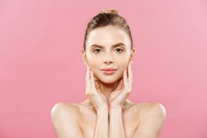 Beauty Spa Concept - Caucasian Woman with perfect face skin Portrait. Beautiful Brunette Spa Girl showing empty copy space. Isolated on pink studio background. Proposing a product. Gesture for advertisement.